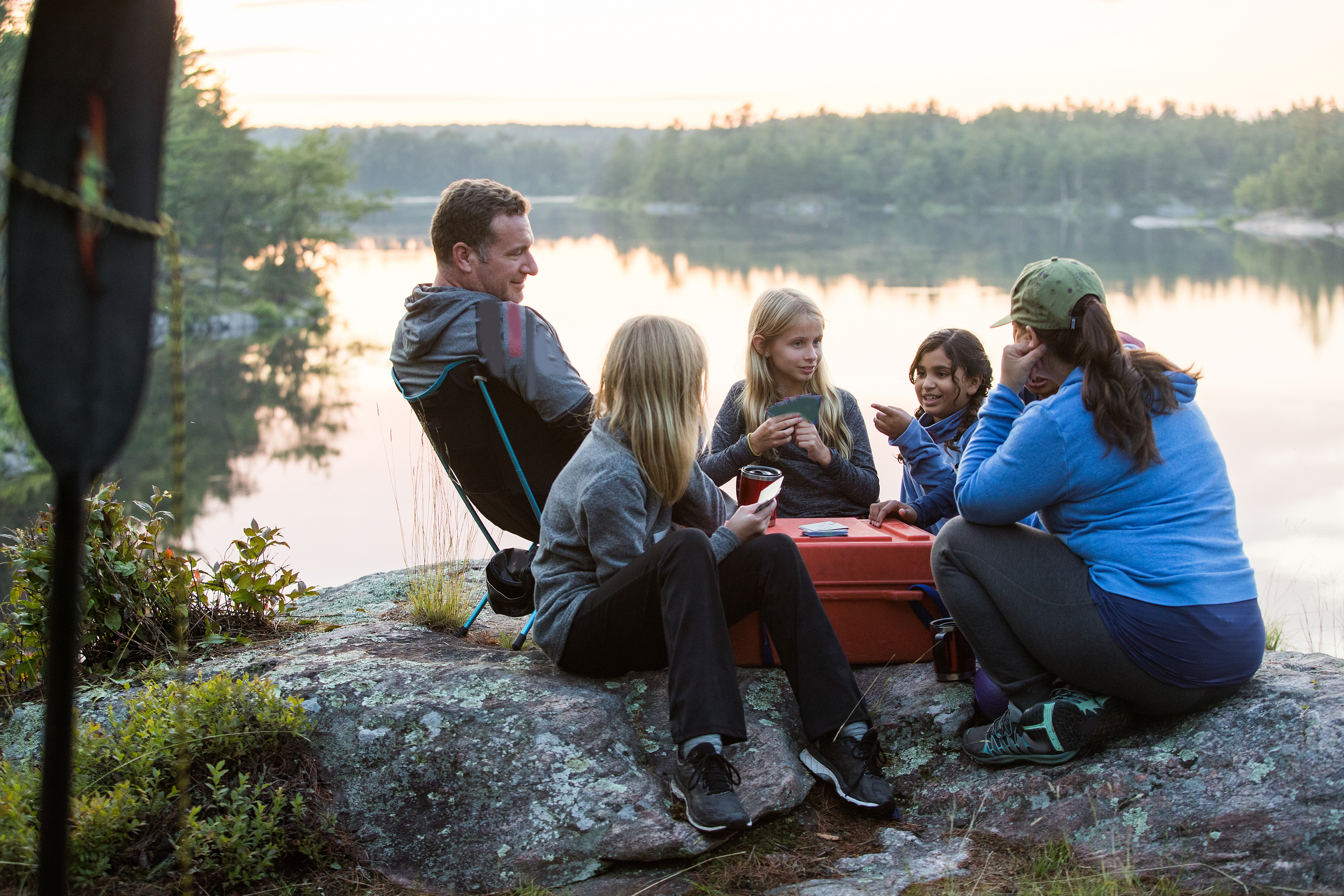 Famille en camping jouant aux cartes au bord de l’eau.